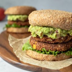 two burgers with lettuce and tomato on a wooden plate