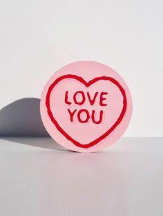 a pink button with the word love you written on it and a red heart in the middle