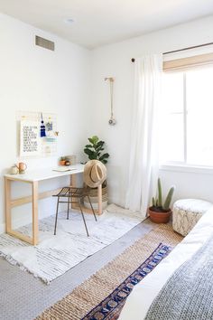 a bedroom with a bed, desk and rug in front of a window on the floor