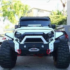 the front end of a white four - door jeep with large tires and lights on