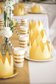 a table topped with yellow cups and vases filled with white flowers next to each other