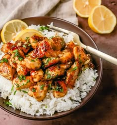 a brown bowl filled with chicken and rice next to lemon wedges on a table