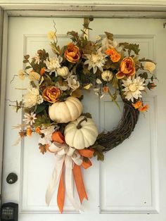 a wreath with flowers and pumpkins hanging on the front door