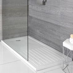 a bathroom with a stand up shower next to a white stool and gray tiled walls