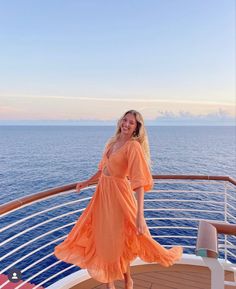 a woman in an orange dress standing on the deck of a cruise ship looking at the camera