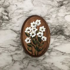 an oval wooden plaque with white flowers on it sitting on a marble countertop in the shape of a flower