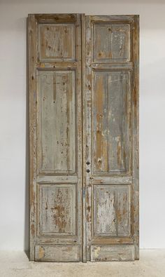 an old wooden double door with peeling paint on the doors and side panels, against a white wall