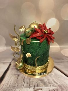 a green and gold christmas cake with poinsettis on top, sitting on a wooden table