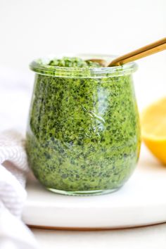 a glass jar filled with green pesto next to a slice of lemon on a white plate