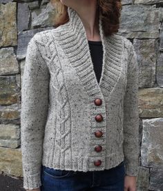 a woman standing in front of a stone wall wearing a sweater with buttons on it