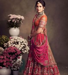 a woman in a pink lehenga standing next to a vase with flowers on it