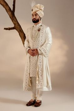 White full sleeves sherwani in linen silk base with all over Kashmiri Jamawar embroidery highlighted wih dabka and zari. Paired with full sleeves plain kurta, churidar, safa and embroidered border stole.
Components: 5
Pattern: Embroidery
Type Of Work: Zari, Dabka
Neckline: Band
Sleeve Type: Long
Fabric: Linen Silk
Color: White
Other Details: 
Closure: 
Sherwani: Front hooks
Kurta: Front placket buttons
Note: The jewellery and kalangi worn by the model is not for sale
Occasion: Groom - Aza Fashio Jatin Malik, White Sherwani, Embroidered Sherwani, Blouse Yoke, Dhoti Pants, Royal Look, Zari Work, Indian Wedding Outfits, Pashmina Shawl