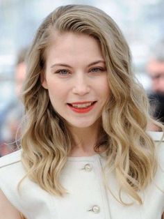 a woman with long blonde hair wearing a white dress and red lipstick is smiling at the camera