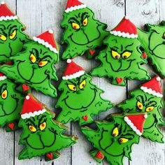 christmas cookies decorated with green and red icing on a white wooden surface, including grin - like faces