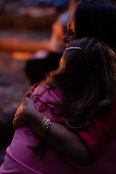 a woman sitting on the ground with her arm around another woman's neck, both arms crossed