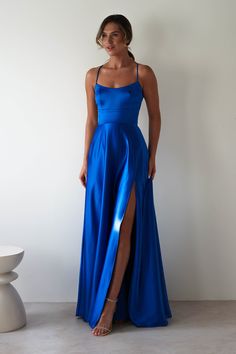 a woman in a long blue dress standing next to a white table with a vase on it