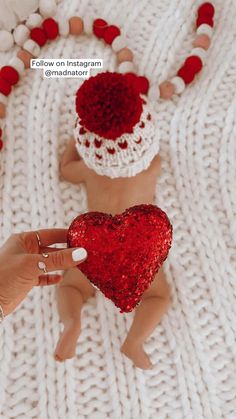 someone is holding a heart shaped object in front of two small baby dolls on a white blanket