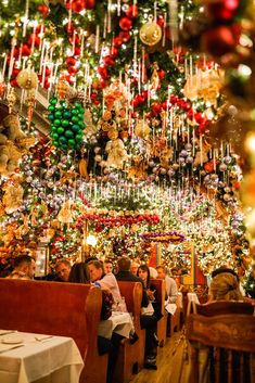 people sitting at tables in front of a christmas tree with lights and ornaments hanging from the ceiling