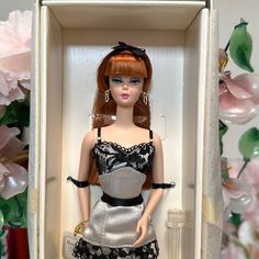 a barbie doll in a box with flowers behind it