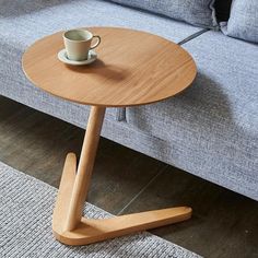 a small wooden table with a cup on it in front of a couch and rug