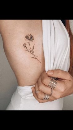 a woman with a flower tattoo on her back and arm, holding onto the side of her body