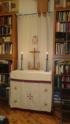 an altar with candles in front of bookshelves and a cross on the table