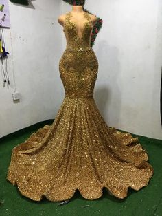 gold sequins mermaid style prom dress with open back and train on display in front of white wall