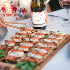 a bottle of wine and some food on a wooden platter with chopsticks