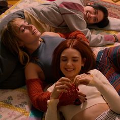 three women laying on a bed with one holding a knitted ball and the other smiling