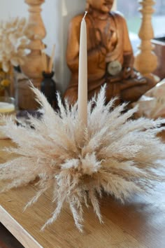 a white candle sitting on top of a wooden table next to a statue and candlestick