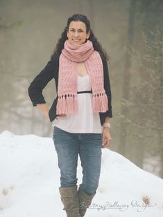 a woman standing in the snow with her hands on her hips wearing a pink scarf