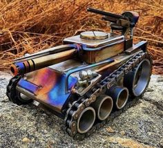 a toy tank sitting on top of a rock next to some dry grass and weeds