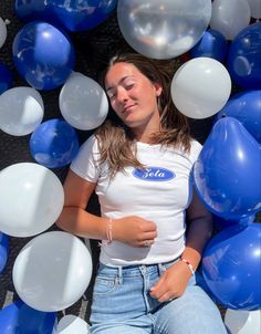 a woman laying on the ground surrounded by blue, white and silver balloons with her eyes closed