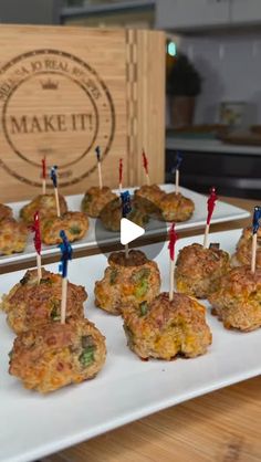 small appetizers with toothpicks are displayed on a white plate in front of a wooden box