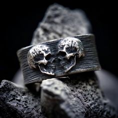 a silver ring with two skulls on it sitting on top of some rocks in the dark