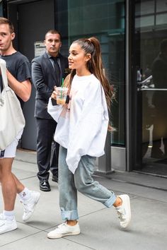 the woman is walking down the street with her hand in her pocket and holding a drink