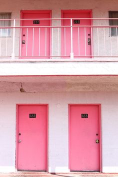 three pink doors in front of a white building with red balconies on the second floor