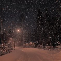 a snow covered road at night with street lights in the distance and trees on either side