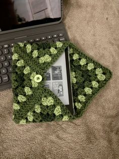 an open laptop computer sitting on top of a bed next to a green crocheted cover