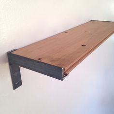 a wooden shelf mounted to the side of a white wall with metal brackets on it