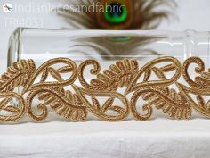 an intricately designed gold brooch sits in a glass container on a table with a peacock behind it