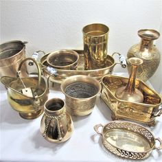 an assortment of antique brass items on a white tablecloth, including cups and saucers