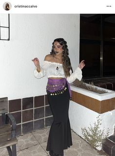 a woman in a costume standing next to a wall with her hands out and pointing at something