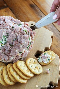 a person is cutting up some crackers on a wooden board with cheese and meat