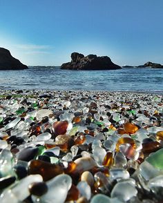 a beach covered in lots of different colored glass pebbles next to the ocean on a sunny day