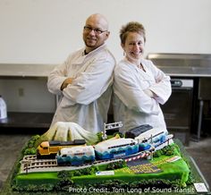 two people standing in front of a cake that looks like a train on the tracks