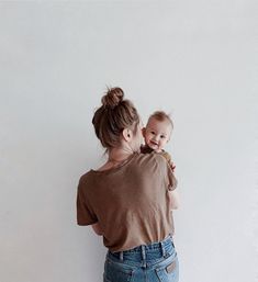 a woman holding a baby up to her chest and looking at the wall behind her