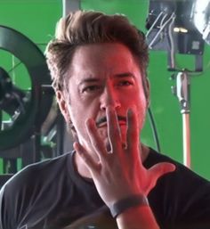 a man with his hand on his face in front of a green screen and camera