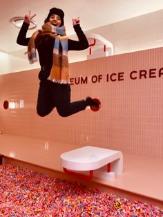 a woman jumping in the air with a scarf around her neck and an ice cream sign behind her