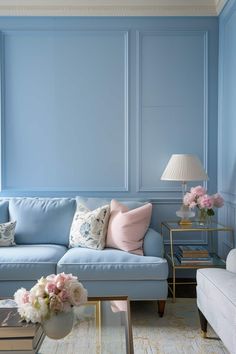 a living room with blue walls and white couches, pink flowers on the coffee table